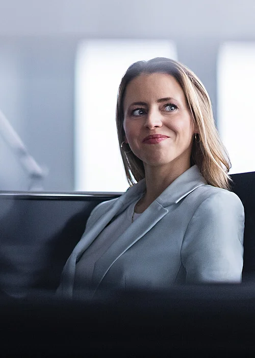 A young business woman who is sitting in an office and has a satisfied smile