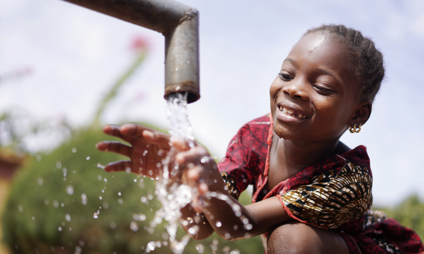A young girl happily running her hand under fresh water