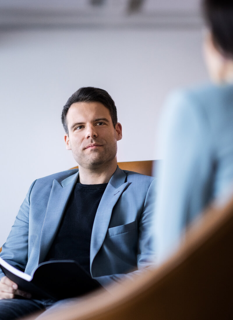 A male office employee sitting and listening attentively to a colleague while holding a notepad